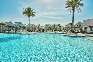 A large outdoor swimming pool with clear blue water, surrounded by lounge chairs and palm trees. - 30A | Golf Cart | Resort Pool | Bikes (Panama City Beach)