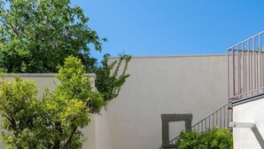 A staircase with a metal railing, a white wall with a small window, and a tree with green leaves. - Charming en-suite room with private terrace (Forio)