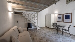 A modern living room with a sofa, a dining table with chairs, a staircase, and a wall with framed pictures. - Charming en-suite room with private terrace (Forio)