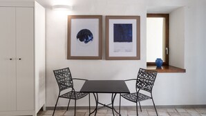 A dining area with a table and chairs, two framed artworks on the wall, and a window with a vase on the sill. - Charming en-suite room with private terrace (Forio)