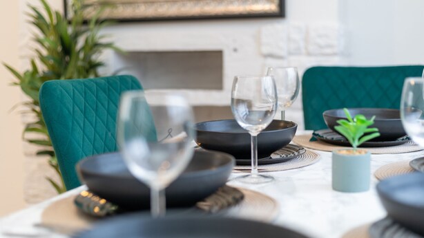 Una mesa de comedor dispuesta con cuencos negros, copas de vino y una pequeña planta.