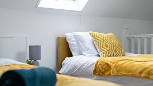 Un dormitorio con una cama, una mesita de noche, una lámpara y una ventana.