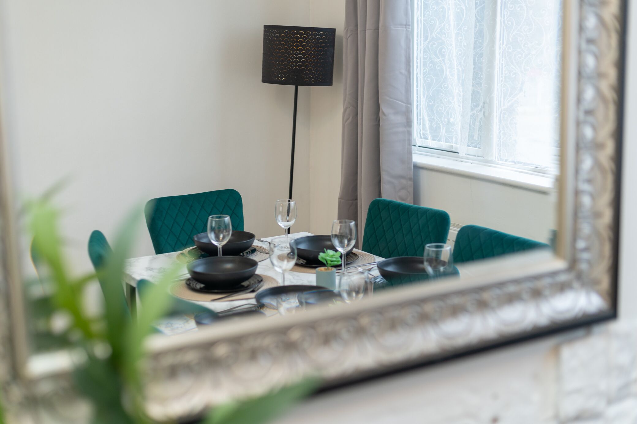 A dining table set with plates, bowls, and glasses, a floor lamp, and a mirror reflecting the room.
