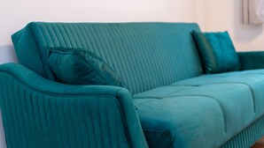 Un sofá tapizado en color verde azulado con textura vertical y dos almohadas a juego frente a una pared lisa.