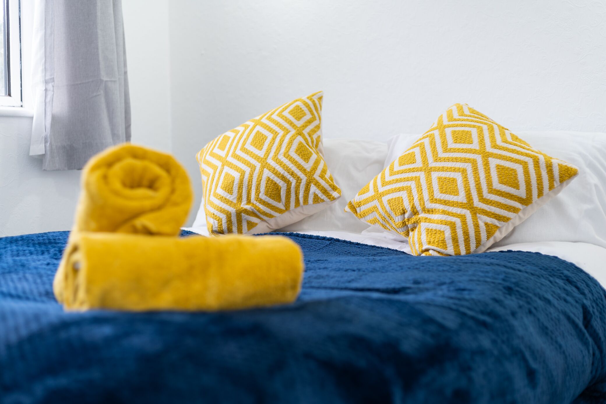 A bed with a blue blanket and two patterned pillows.