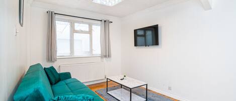 Una sala de estar moderna con un sofá color turquesa, una mesita de centro y un televisor montado en la pared.