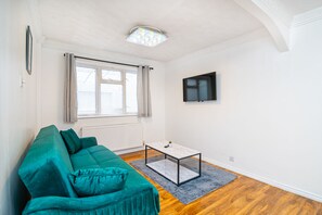 A modern living room with a teal sofa, a small coffee table, and a television mounted on the wall. - Impeccable 3-bed House in Abbeywood (London)