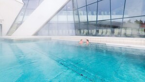 Une piscine intérieure à l’eau d’un bleu limpide, entourée de grandes baies vitrées et dotée d’une architecture moderne.