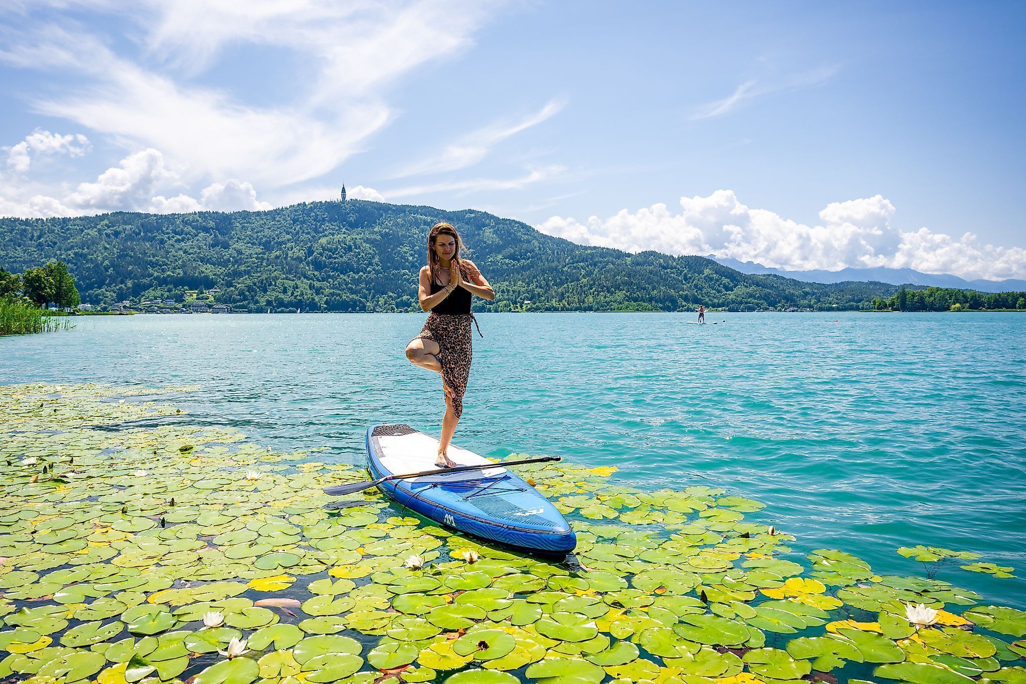 Eine Person steht auf einem Paddleboard auf einem See, umgeben von Seerosenblättern.