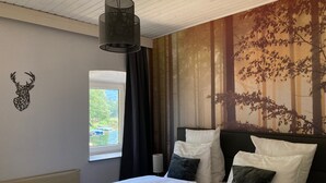 Une chambre avec deux lits, une décoration murale représentant une tête de cerf, une fenêtre avec des rideaux et une fresque murale sur le thème de la forêt.