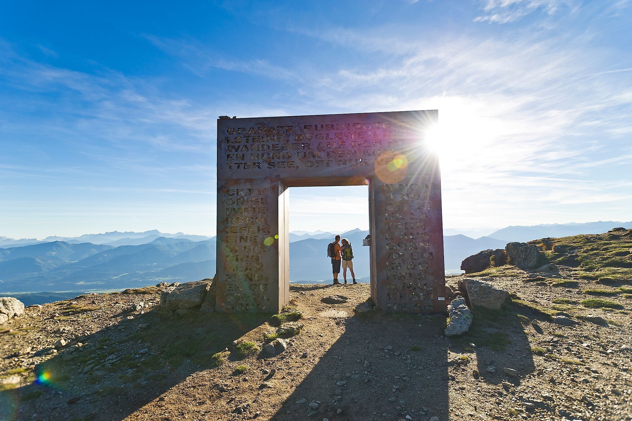 Un arc en pierre orné d’inscriptions, qui mène à un paysage montagneux.