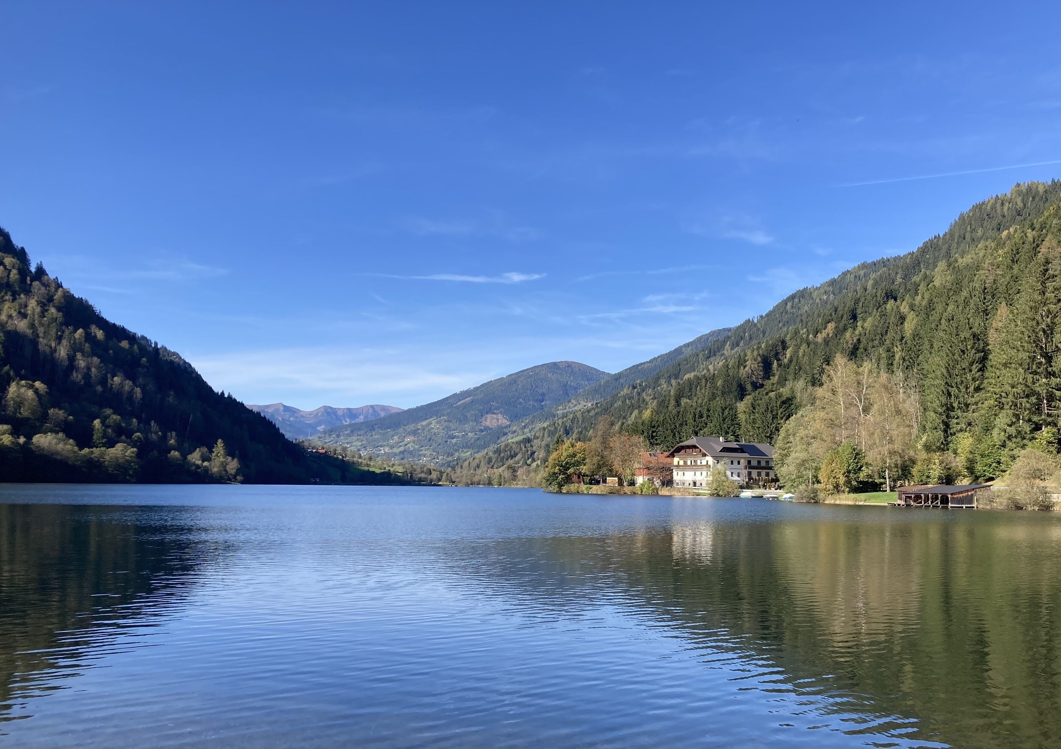 A serene lake with a house on the shore, surrounded by forested hills.