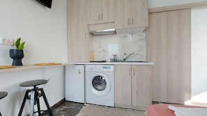 Et kompakt køkken med en indbygget vaskemaskine, et lille spiseområde og en enkelt stol.