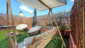 En gårdhave med hængekøje, to polstrede stole, et bord og en pergola med et hvidt tag.