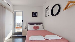 Et soveværelse med seng, et natbord, et vindue og en dør, der fører til en balkon.