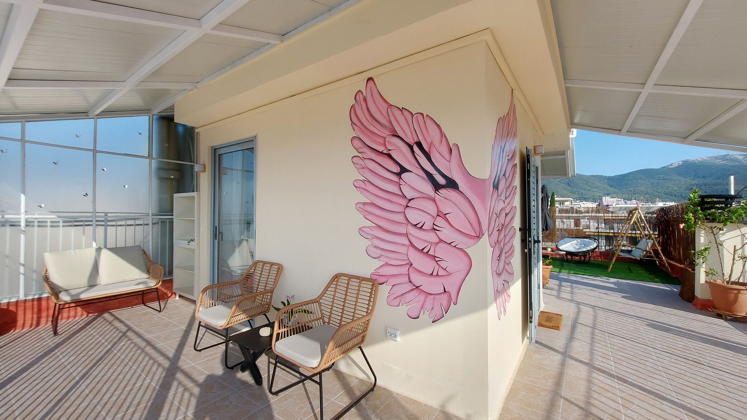 Un balcón con sillas de mimbre, un mural grande y vistas a las montañas.