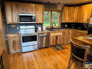 Una cocina con armarios de madera, electrodomésticos de acero inoxidable, una ventana con vistas y un taburete de bar.