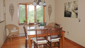 A dining room with a wooden table and chairs, a chandelier, and a large window with a view of trees. - Welcome to Howe Hill Retreat! (Great Valley)