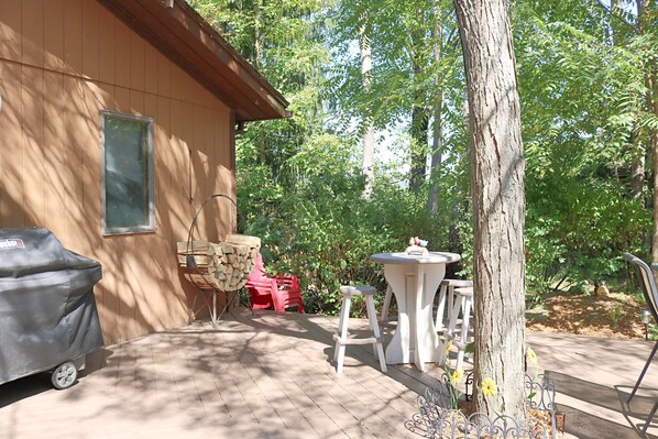 A wooden deck with a barbecue grill, outdoor furniture, and a tree.