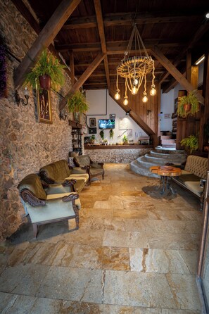 A rustic interior with stone walls, wooden beams, leather sofas, a stone floor, and a chandelier. - KOLAĞASI KONAK (Safranbolu)
