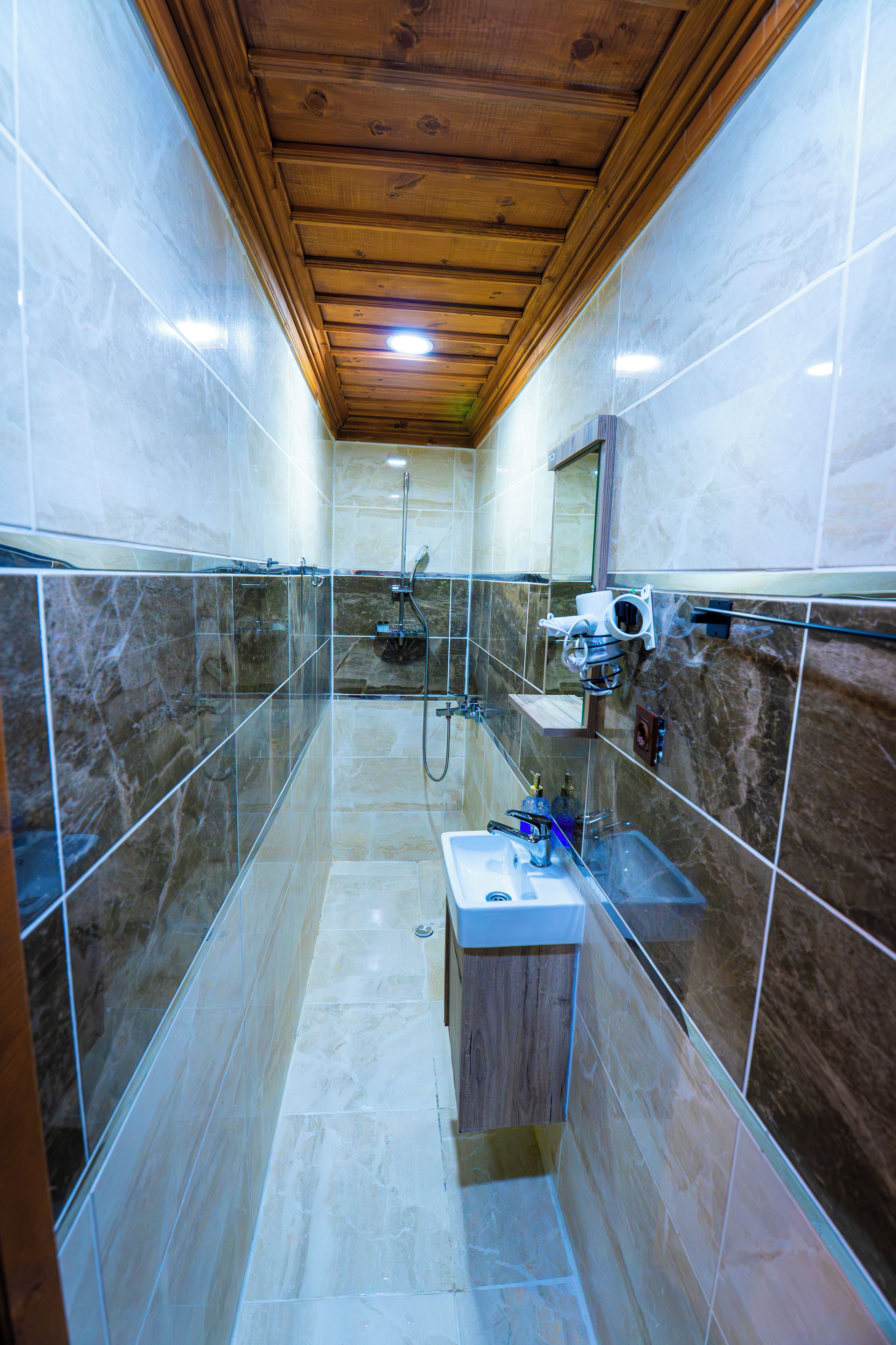 A narrow bathroom with a shower, a sink, and a mirror.