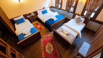 A hotel room with three beds, a wooden floor, a red patterned rug, and a window with curtains.