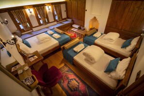 A room with four beds arranged in a U-shape, each with a pillow and a folded towel. There is a small table with a lamp and a chair. - KOLAĞASI KONAK (Safranbolu)
