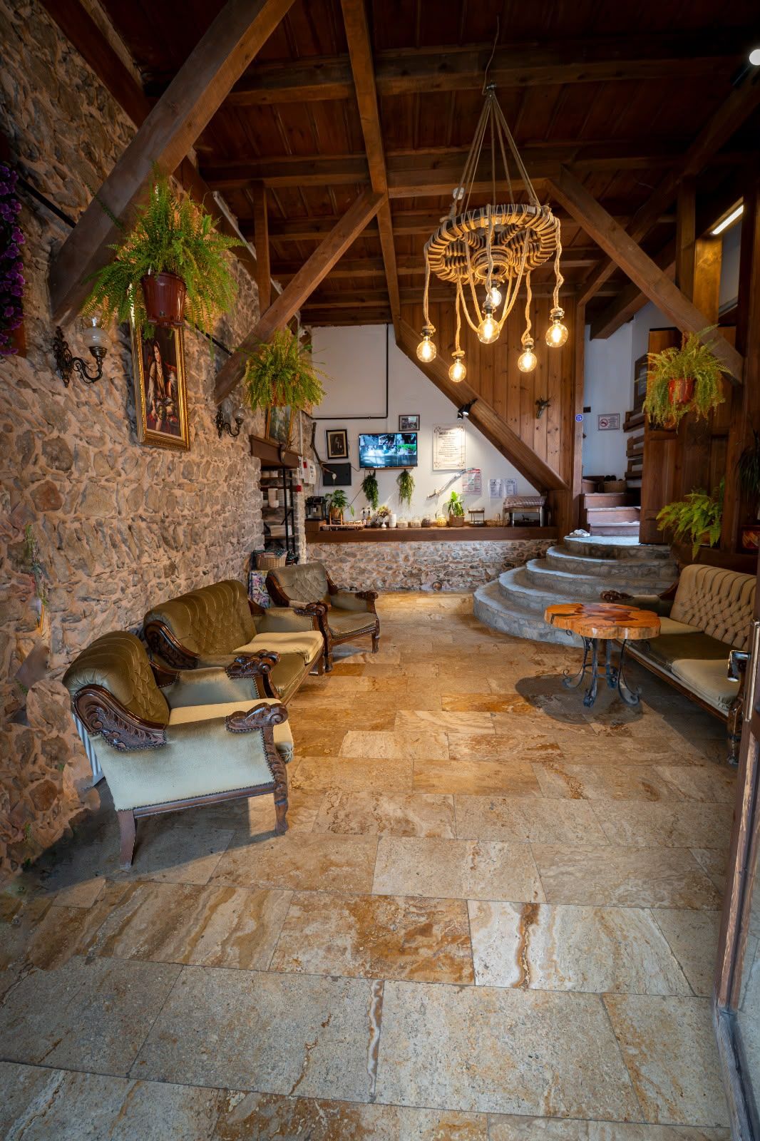 A rustic interior with stone walls, wooden beams, and a stone floor. There are leather sofas and a wooden table.