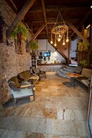 Un interior rústico con paredes de piedra, vigas de madera y suelo de piedra. Hay sofás de cuero y una mesa de madera.