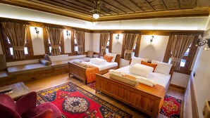 A room with two beds, a wooden bench, a red chair, and a patterned rug. - KOLAĞASI KONAK (Safranbolu)
