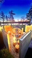 A cozy outdoor seating area with a fire pit, surrounded by wooden structures and trees, overlooking a scenic landscape.