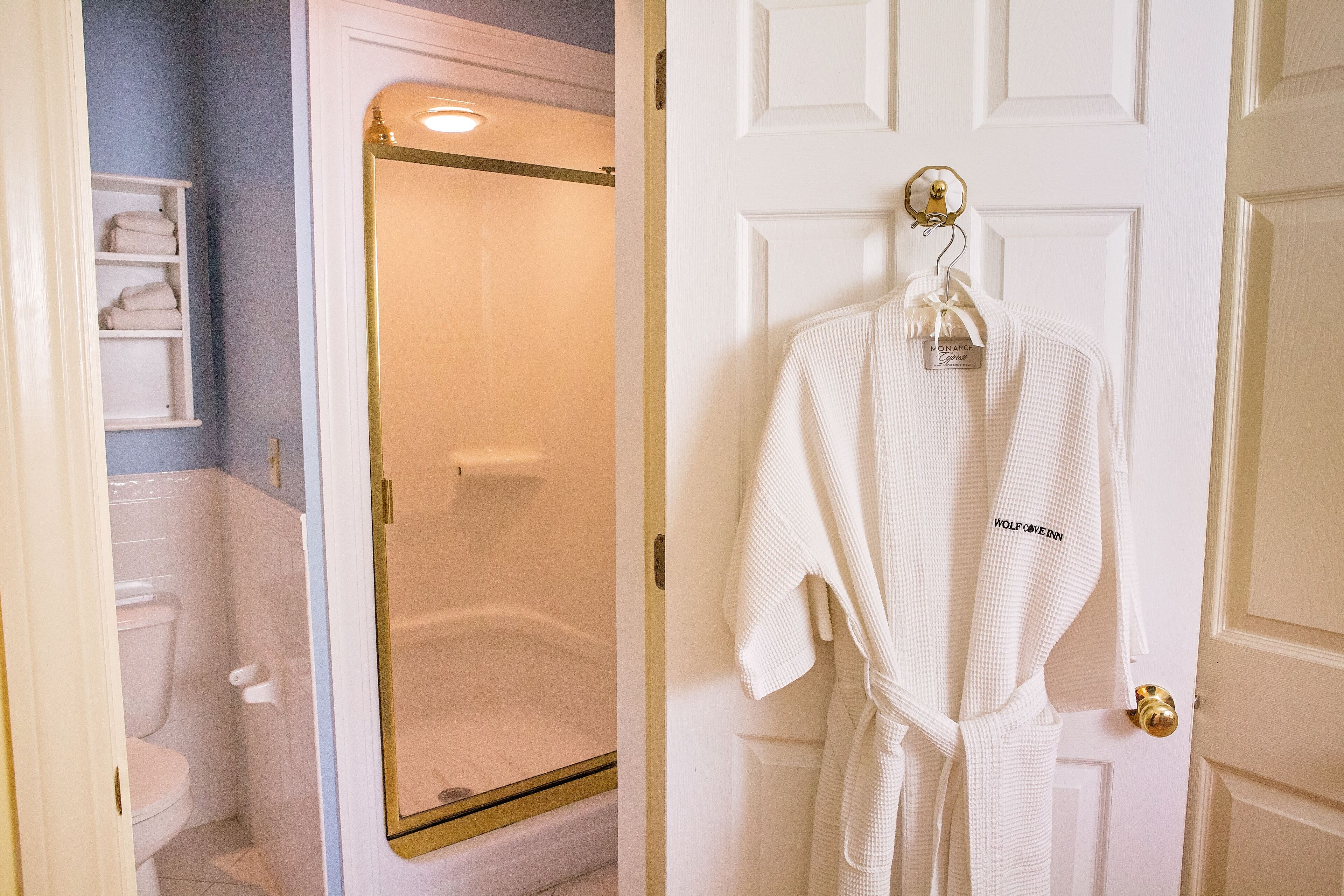 Un baño con una bañera blanca, un inodoro blanco y una bata blanca colgada de una puerta.