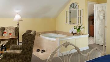 A bedroom with a large bathtub, a vanity with a mirror, a bed, and a table with two glasses of red wine.