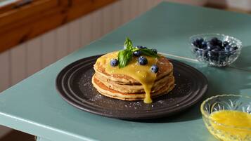 A stack of pancakes on a plate with blueberries and a basil leaf on top, on a teal table.
