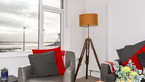 Un salon moderne avec vue sur la plage, un lampadaire et deux canapés ornés de coussins rouges et gris.