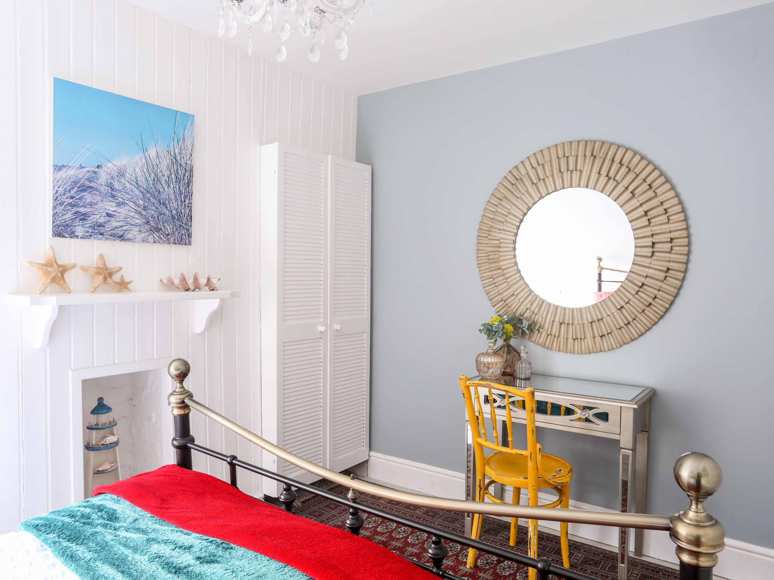 A bedroom with a bed, a desk, a chair, a mirror, and a fireplace.