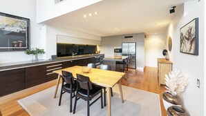 A modern kitchen with dark cabinetry, a central island, and a dining area with a wooden table and chairs. - Lakefront Apartment close to town (Wānaka)
