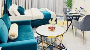 A modern hotel room with a bed, a sofa, a dining table with chairs, and a TV mounted on the wall.