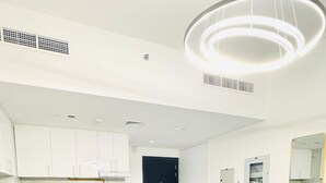 A modern hotel room with a bed, a sofa, a dining table, and a kitchenette.