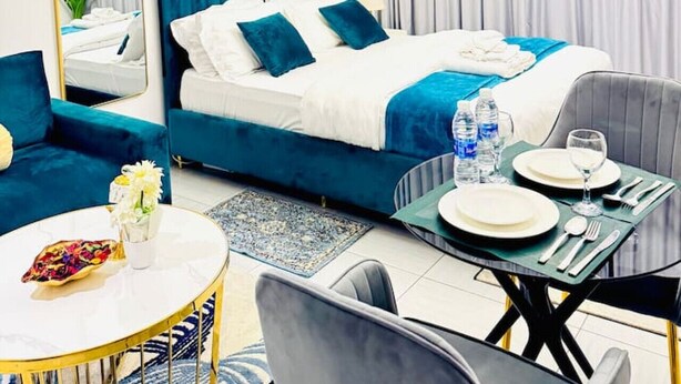 A modern hotel room with a bed, a sofa, a dining table set for two, and a large mirror.