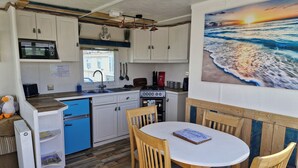 A compact kitchen with white cabinets, a microwave, a sink, and a stove. There's a dining area with a round table and wooden chairs. - Driftwood Cabin Dog Friendly - Anderby Creek (Skegness)