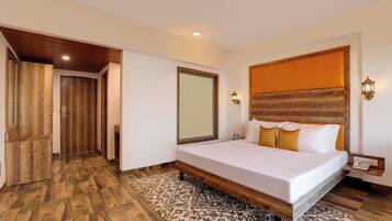 A bedroom with a wooden floor, a bed with white bedding, a headboard with an orange panel, and a patterned rug.