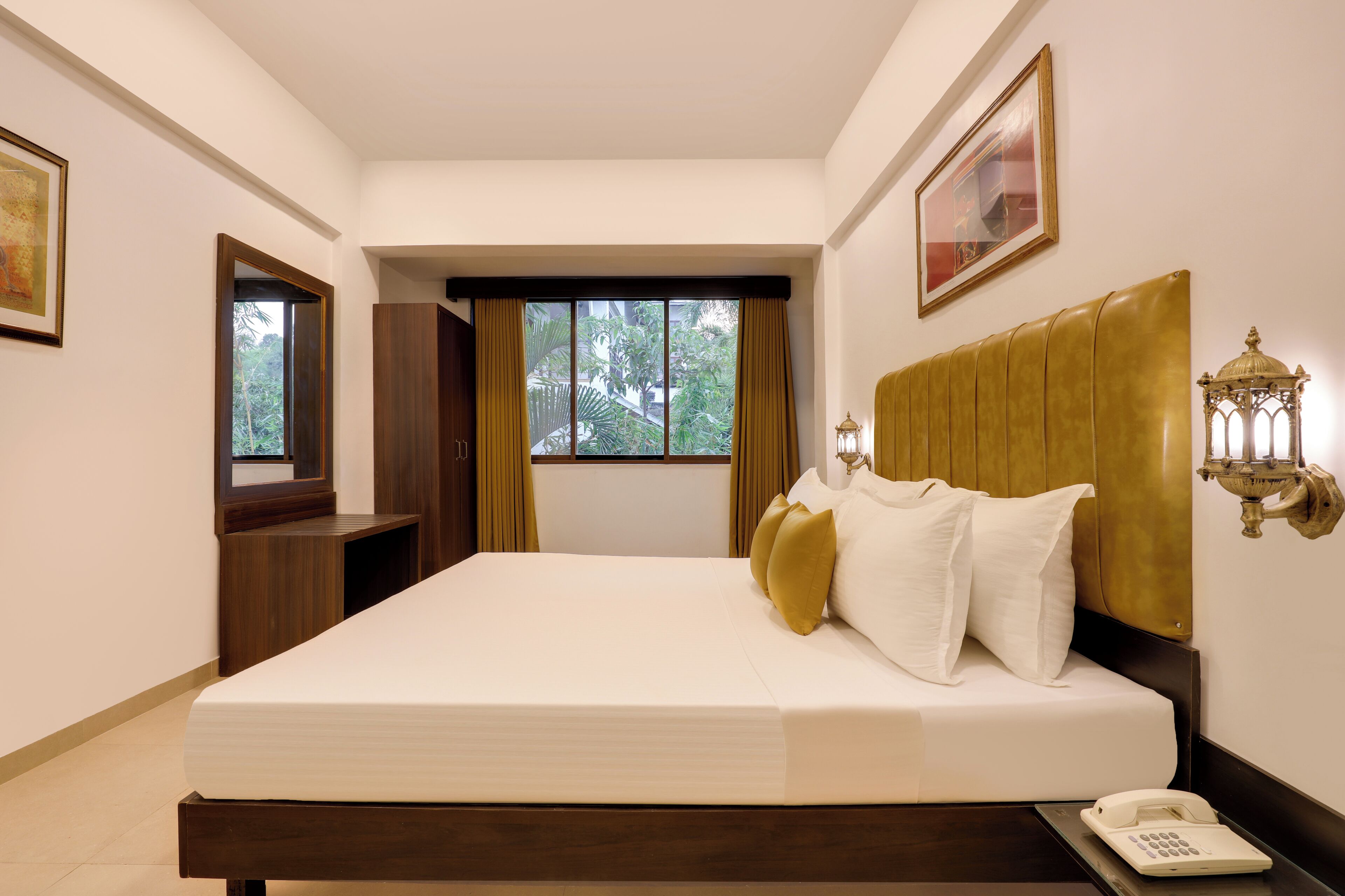 Een hotelkamer met een groot bed, een bedtafeltelefoon, een raam met gordijnen, een wandlamp en een lijst met een afbeelding boven het bed.