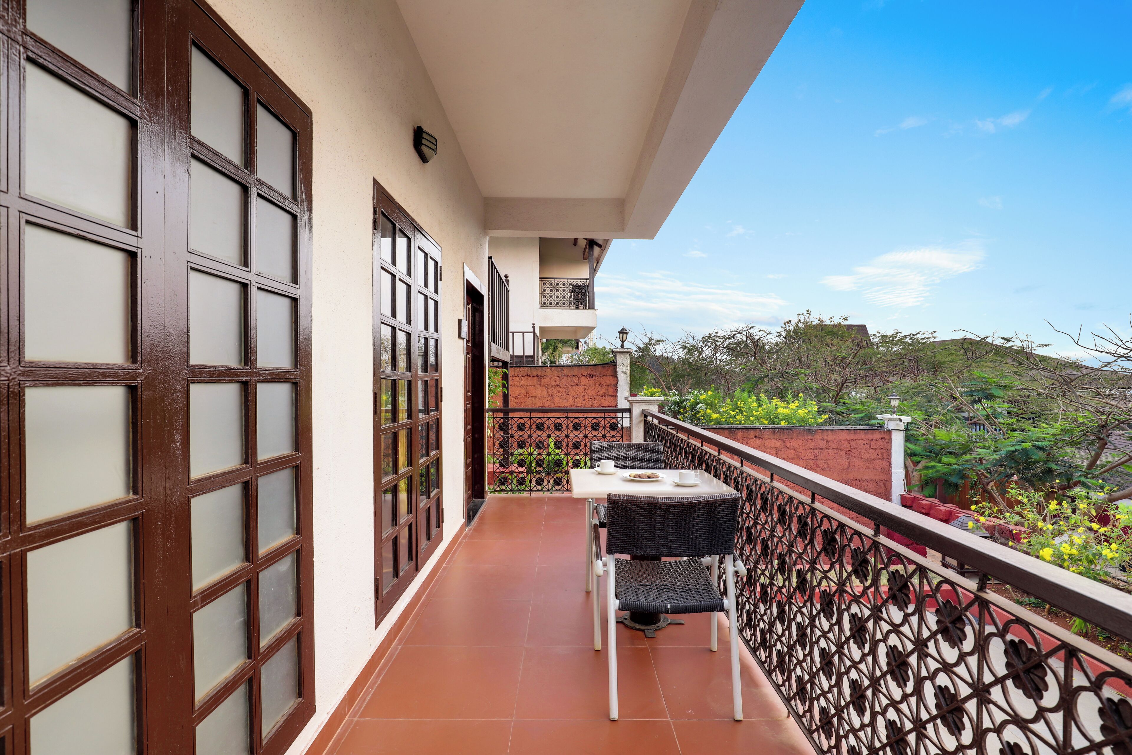 A balcony with a table and chairs, a view of greenery, and a building with a tiled balcony.