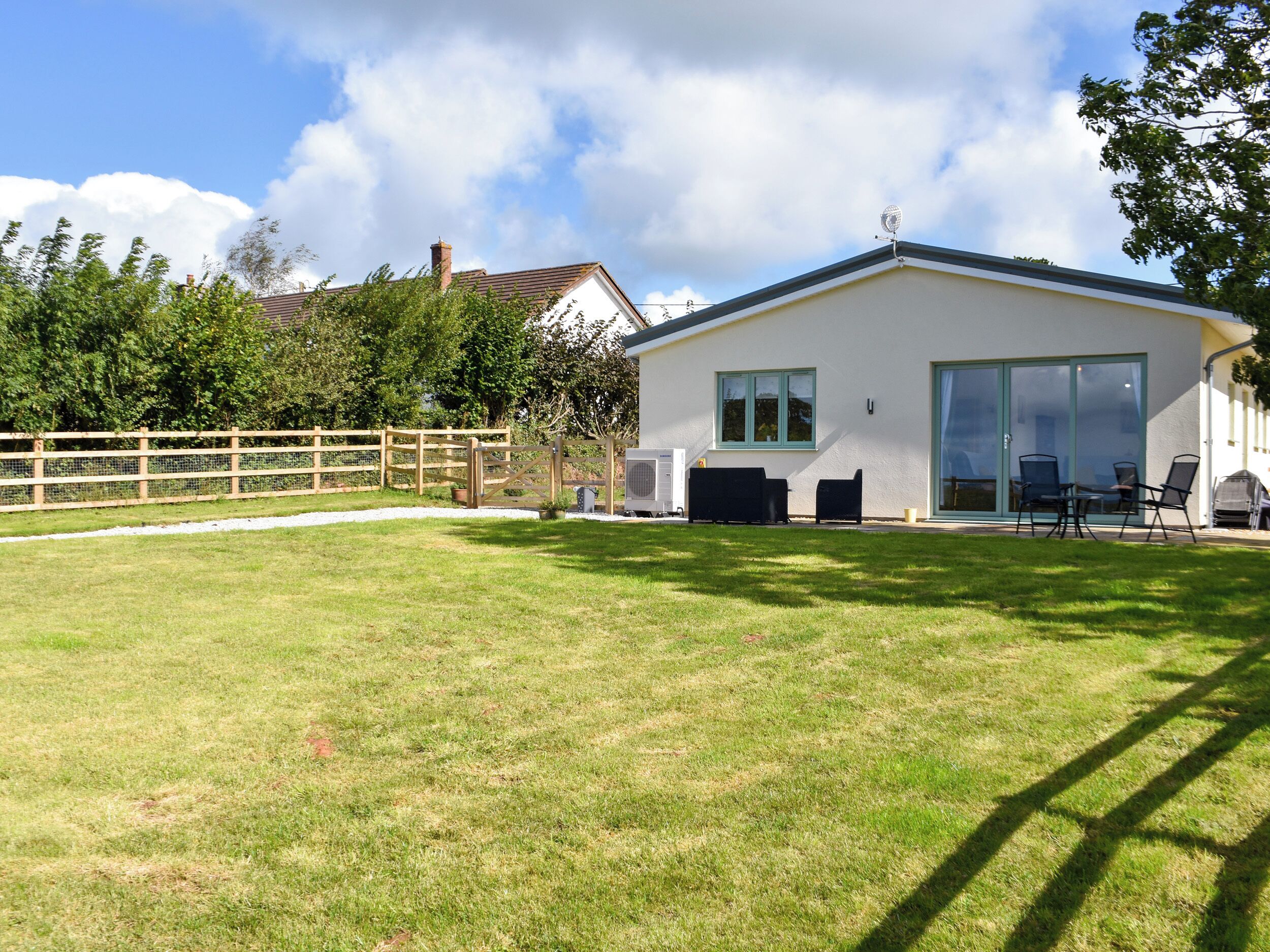 A modern house with a large lawn, a wooden fence, and a patio with outdoor furniture.