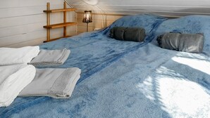 Een bed met een blauwe deken, twee kussens en een houten ladder tegen de muur.