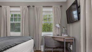 Une chambre à coucher avec un lit, un bureau, une chaise, une télévision et une fenêtre avec des rideaux.