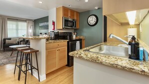 Une cuisine compacte équipée d’un four à micro-ondes, d’une cuisinière et d’un évier. Elle comprend des armoires en bois et un comptoir en granit.