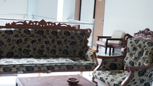 A room with a wooden sofa and armchairs, a small table, and a window with blinds.