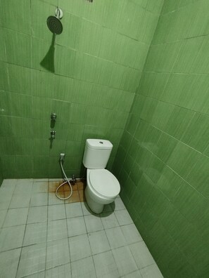 Et badeværelse med grønne fliservægge, et hvidt toilet og et brusehoved.